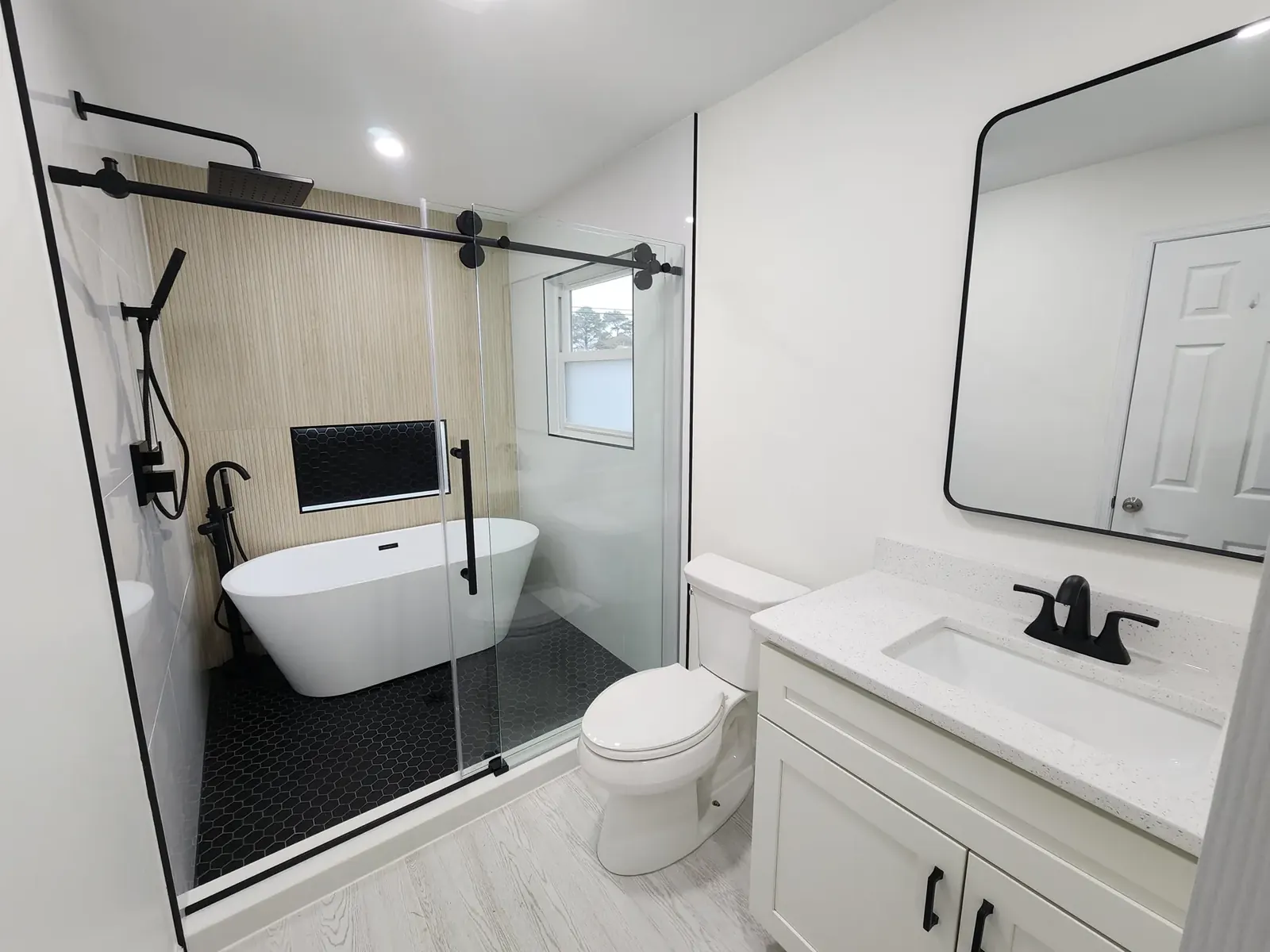 White vanity with a stone top next to a glass-enclosed freestanding tub